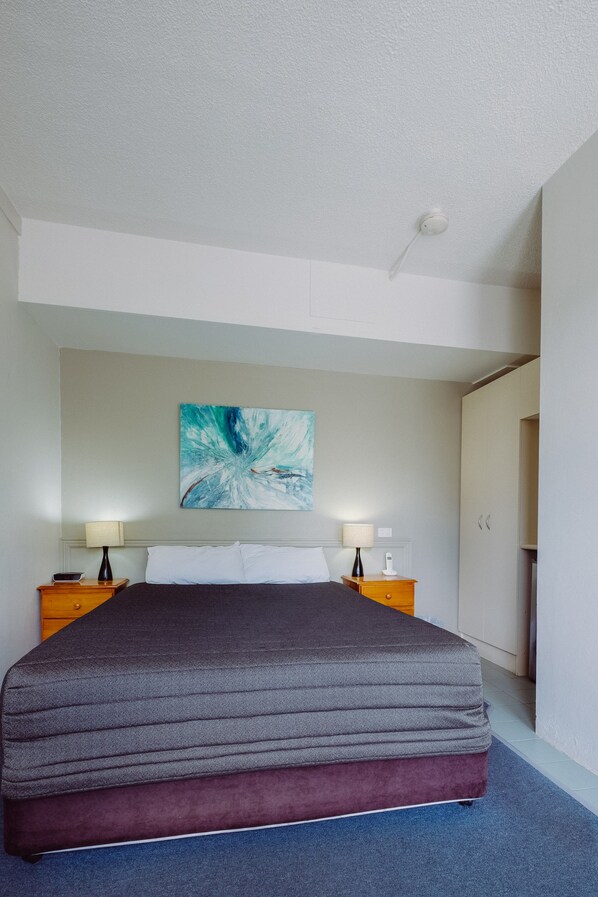 A modern hotel room with a large bed, two bedside tables with lamps, a ceiling light, and a large abstract painting on the wall.