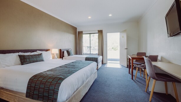 A hotel room with two beds, a desk, chairs, a TV, and a door leading to a balcony. - Artesian Spa Motel (Moree)