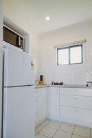 Una cocina con armarios blancos, un refrigerador, un microondas y una ventana con persianas.