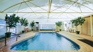 An indoor swimming pool with a covered roof, surrounded by potted plants and a bench. - Artesian Spa Motel (Moree)