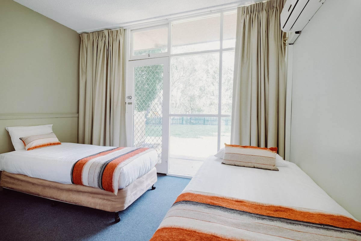 A hotel room with two beds, a large window, and an air conditioning unit.