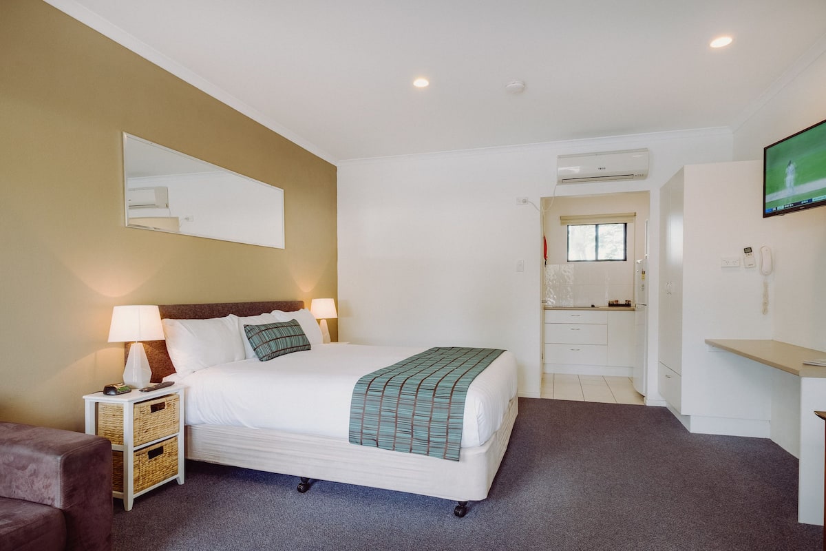 A hotel room with a bed, bedside lamps, a TV, a mirror, a wardrobe, and a small seating area.