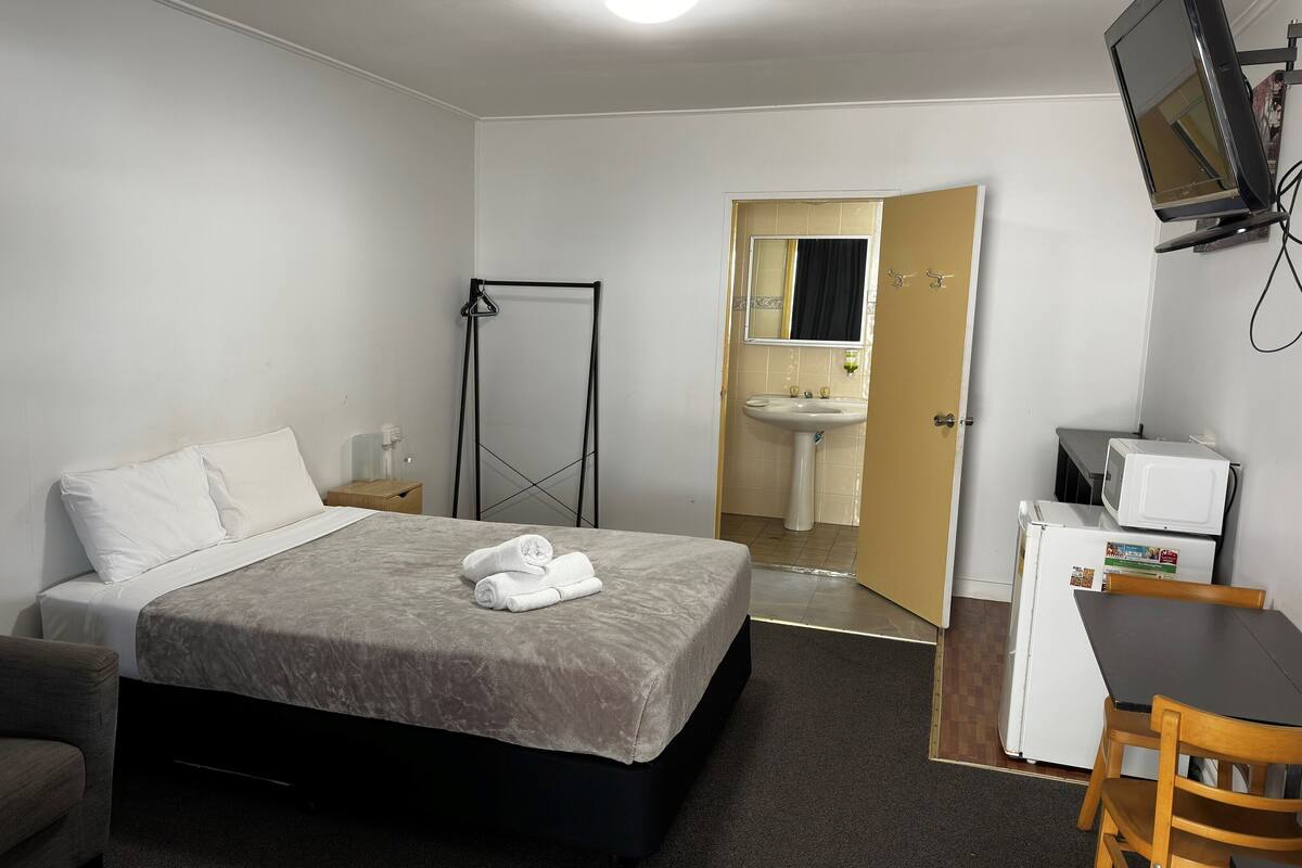 Une chambre d’hôtel équipée d’un lit, d’une chaise, d’un bureau, d’une télévision, d’un lavabo et d’un miroir.