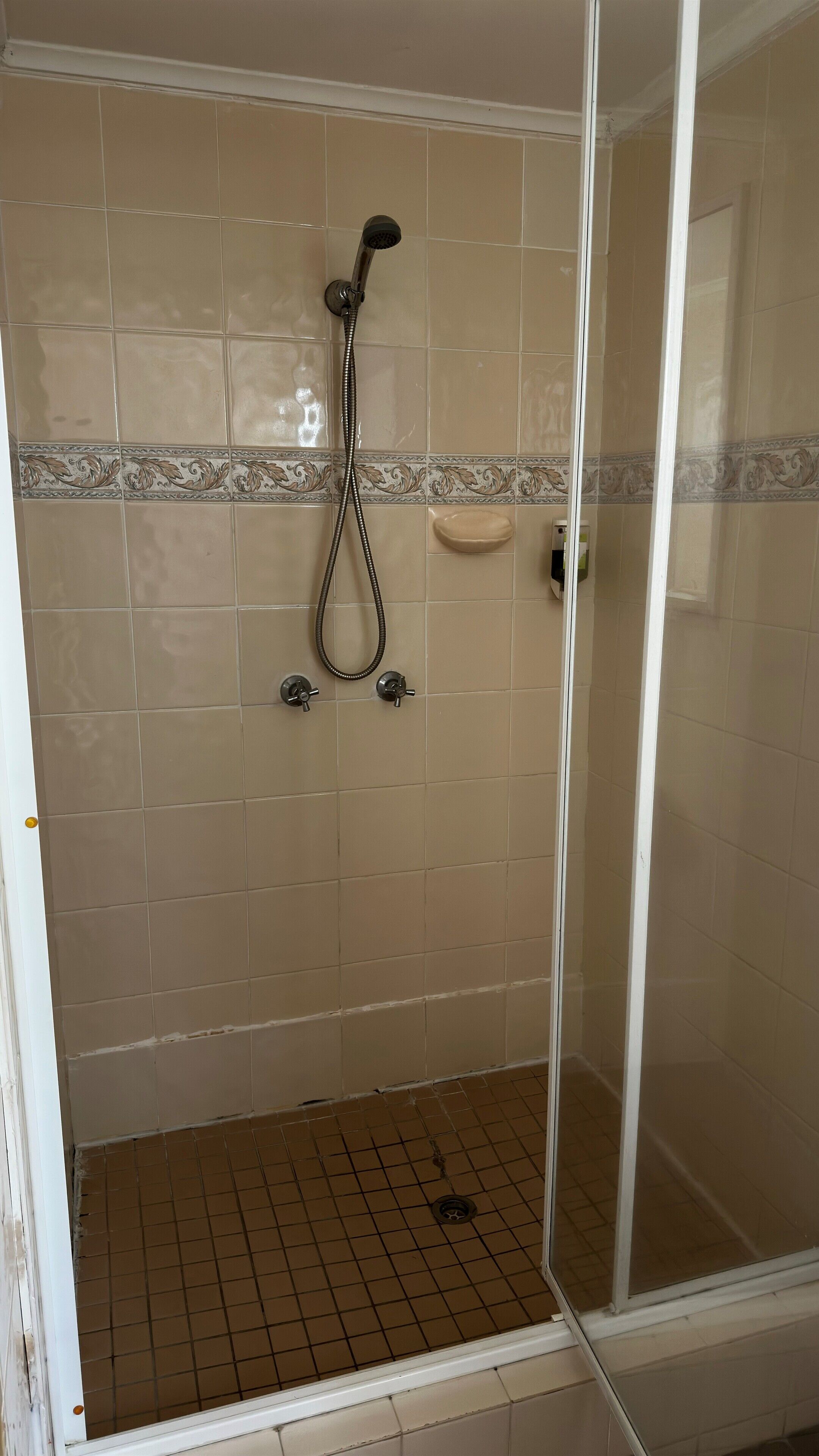 A glass-enclosed shower area with beige tiles and a decorative border.