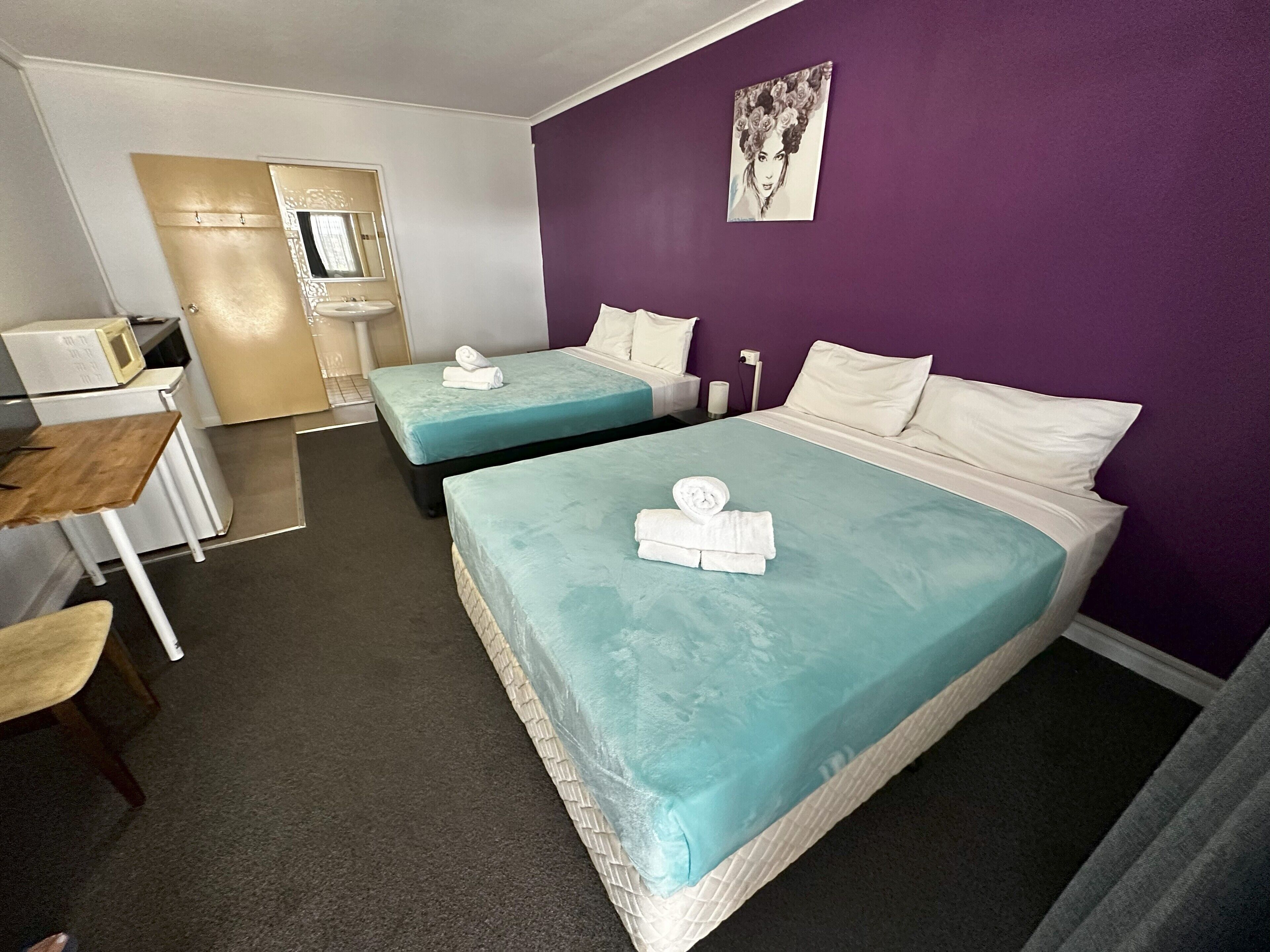 A hotel room with two beds, a desk, a chair, a sink, and a mirror.