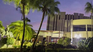 A modern hotel with a circular central building, palm trees, and a statue in the foreground. - The Q Motel (Allenstown)