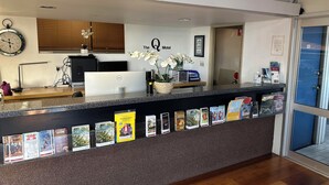 A hotel reception desk with a computer, a clock, and brochures. - The Q Motel (Allenstown)