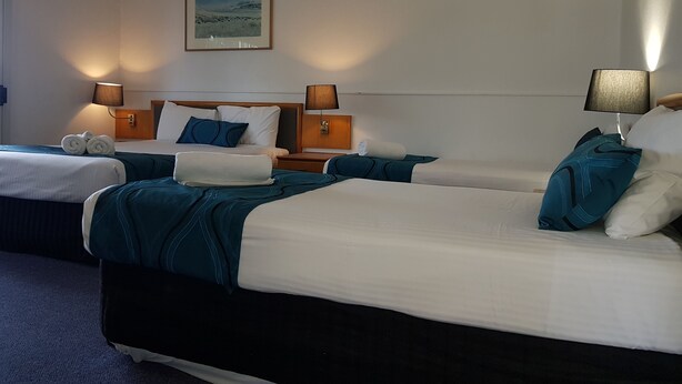 A hotel room with two beds, each with a headboard, bedside tables, lamps, and towels. - The Q Motel (Allenstown)