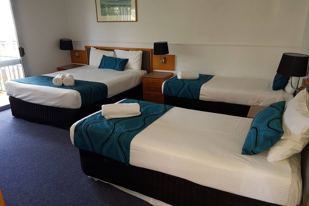 Une chambre d’hôtel avec deux lits, chacun recouvert d’une couvre-lit bleue et blanche, et dotée d’une tête de lit en bois. Il y a deux tables de chevet avec des lampes, et une fenêtre donnant sur l’extérieur.