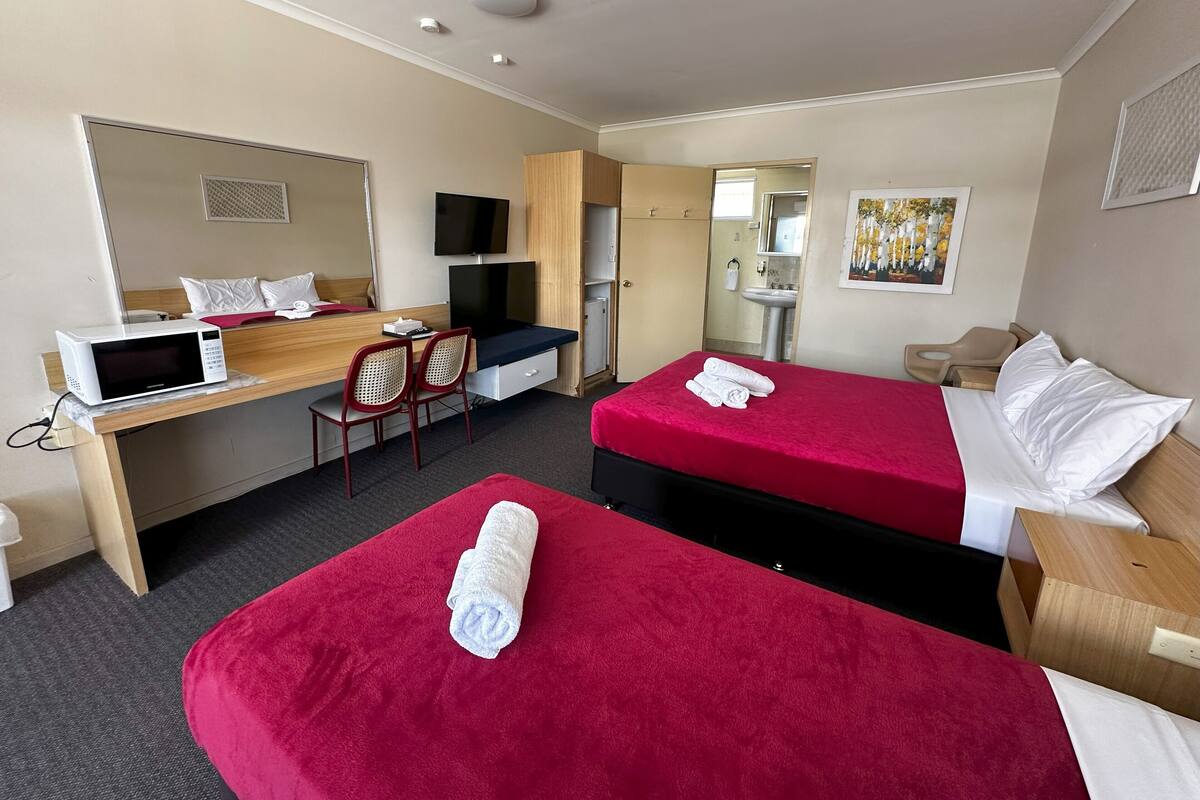 Une chambre d’hôtel avec deux lits, un bureau équipé d’un ordinateur et d’un micro-ondes, une télévision, une salle de bain et un tableau accroché au mur.