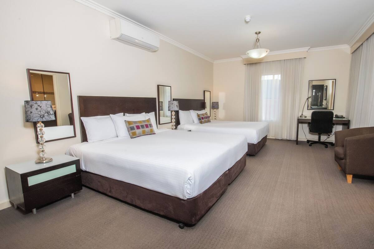 A hotel room with two beds, a desk, a chair, and a large mirror.