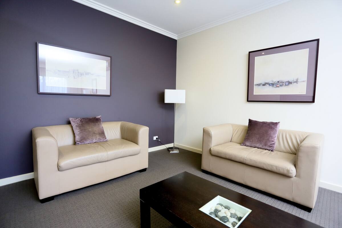 A room with two beige sofas, a dark wooden coffee table, and two framed pictures on the walls.