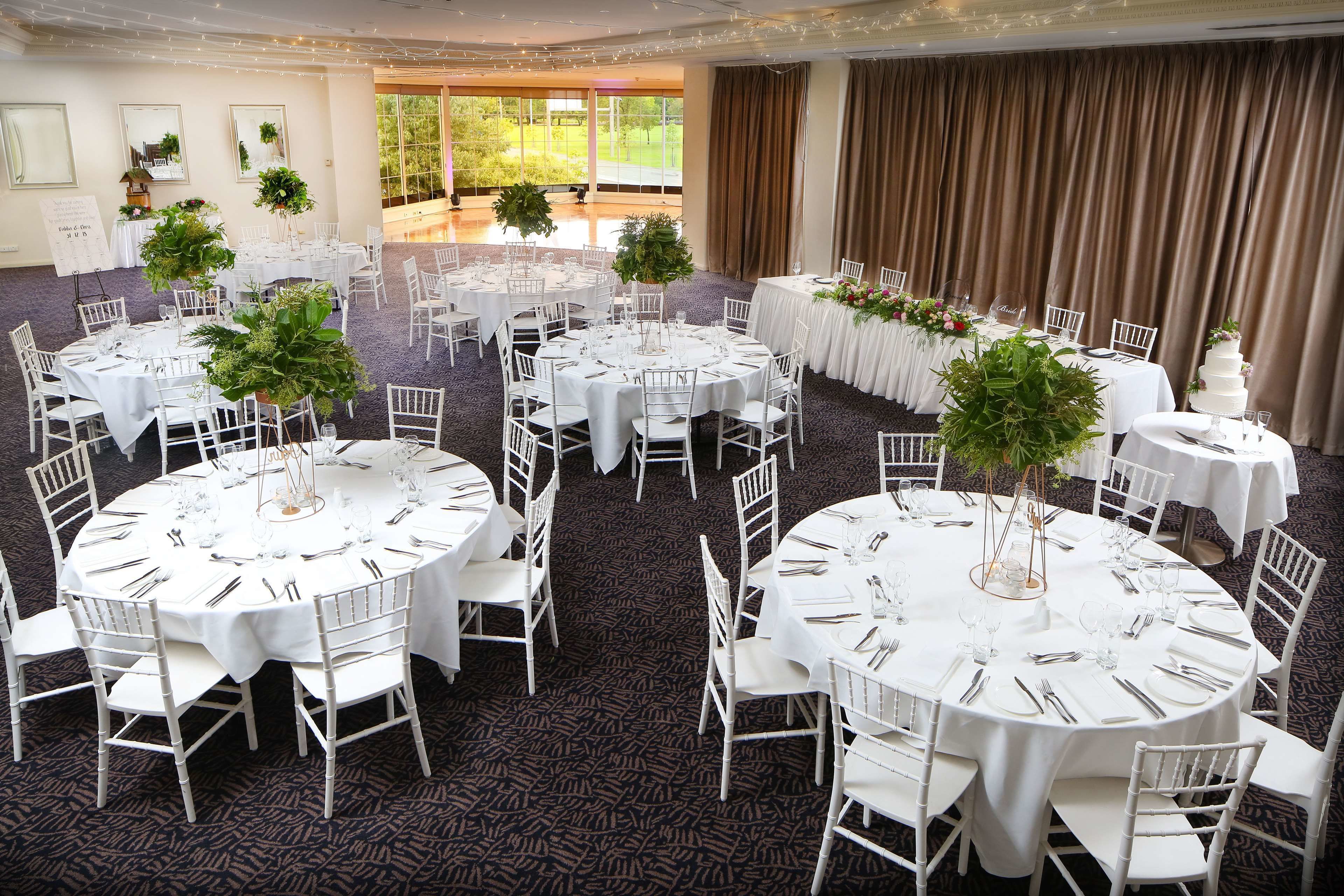 A banquet hall with round tables, white chairs, and floral centerpieces.