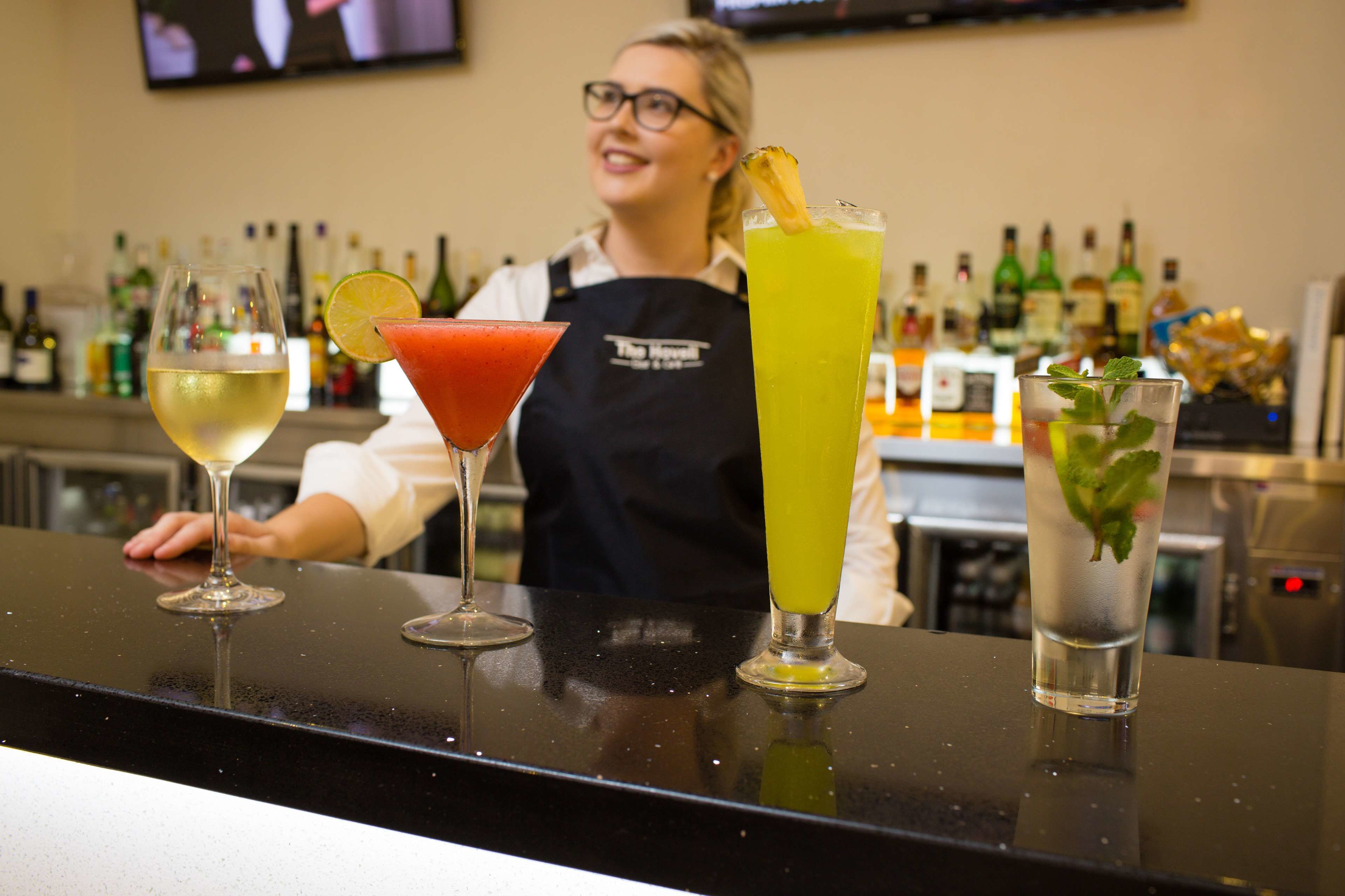 Un bar con tres bebidas sobre la barra y un cantinero al fondo.