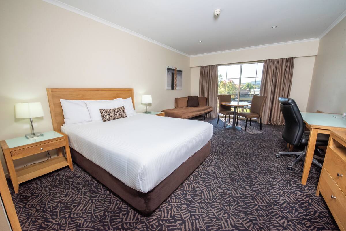 A hotel room with a large bed, a desk, a chair, and a small table.