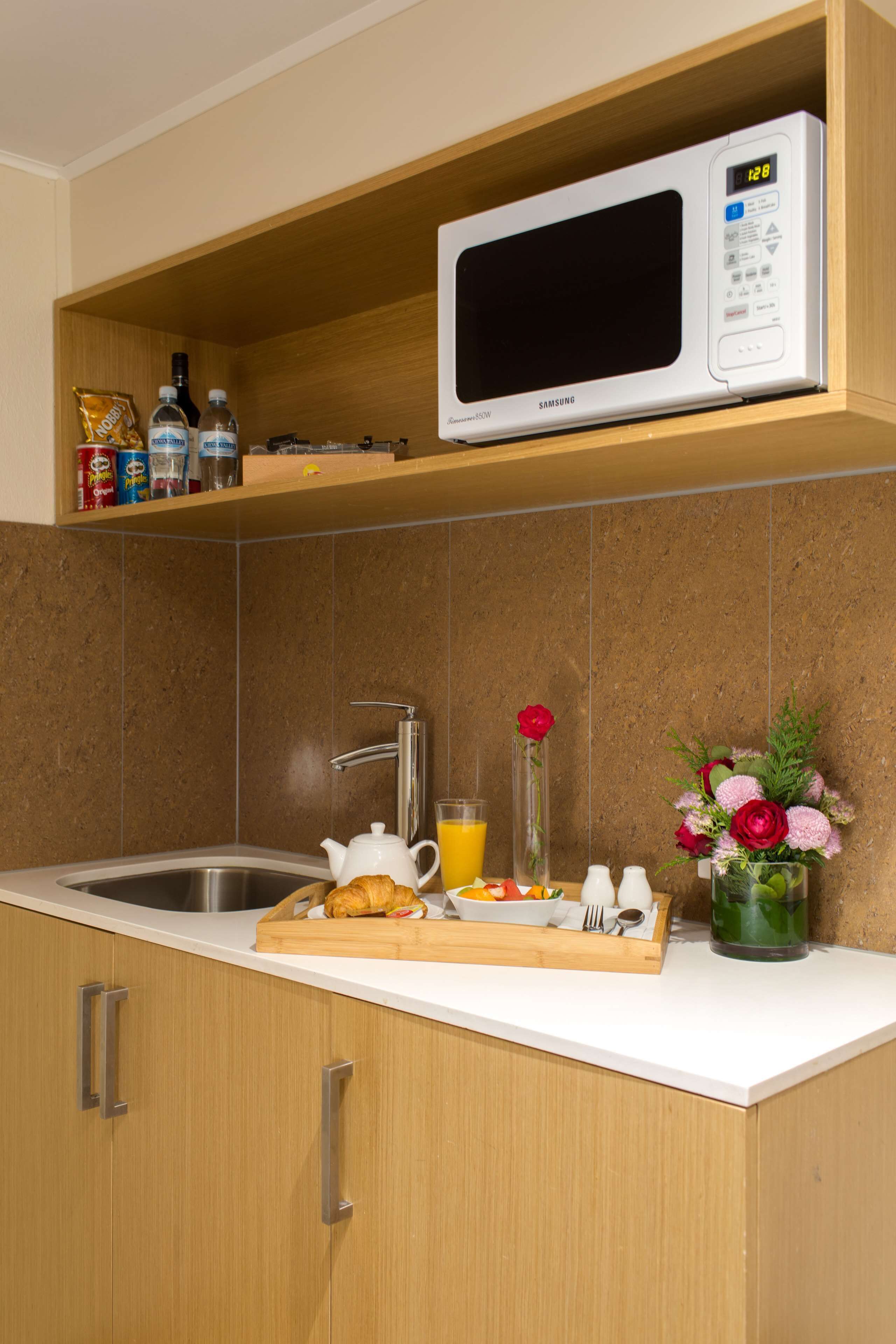 A kitchen with a microwave, sink, and wooden cabinets.