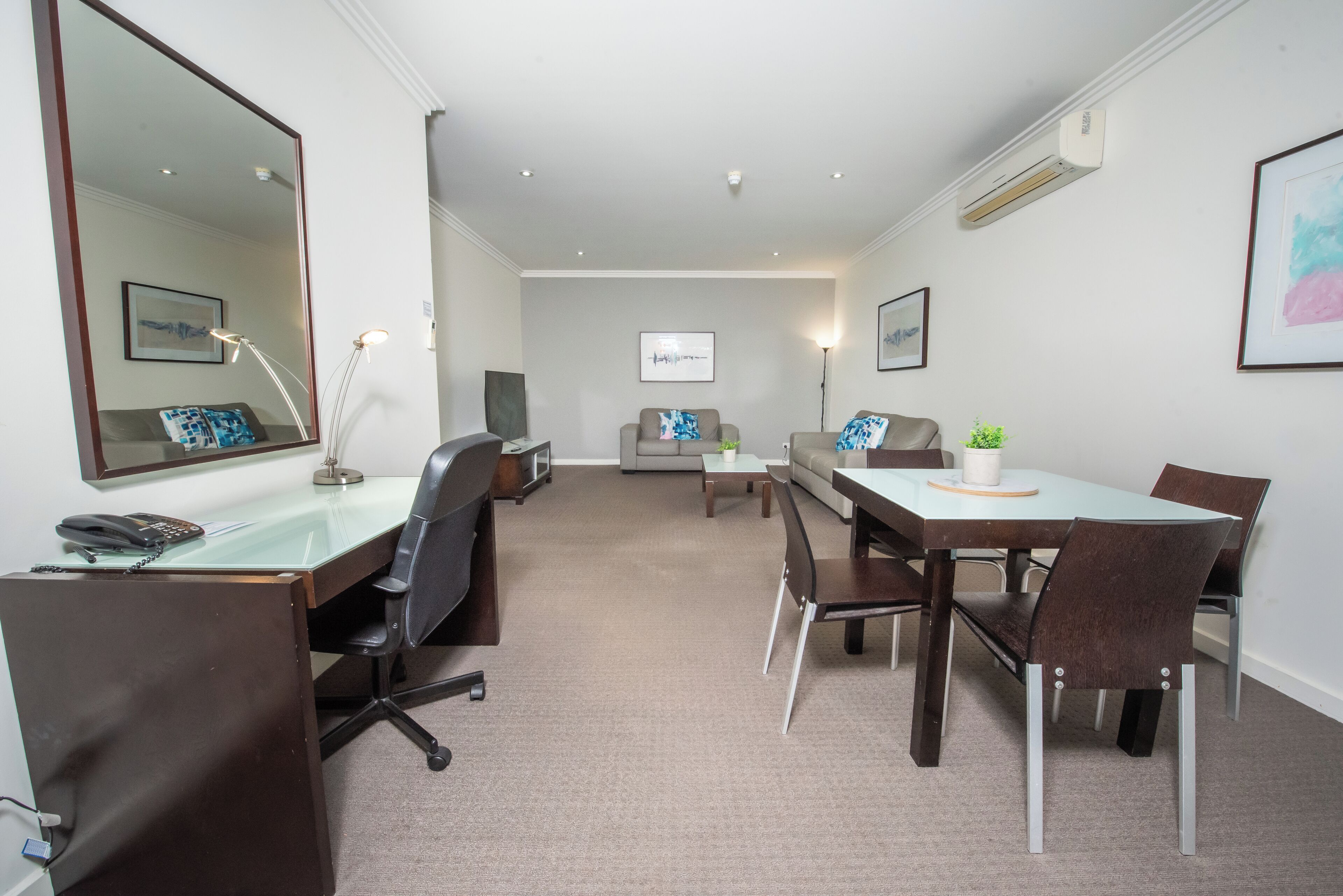A modern hotel room with a large desk, two chairs, a sofa, and a dining table.