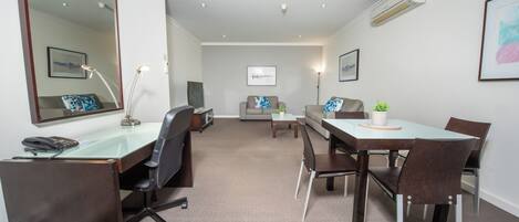 Een moderne hotelkamer met een groot bureau, twee stoelen, een bank en een eettafel.