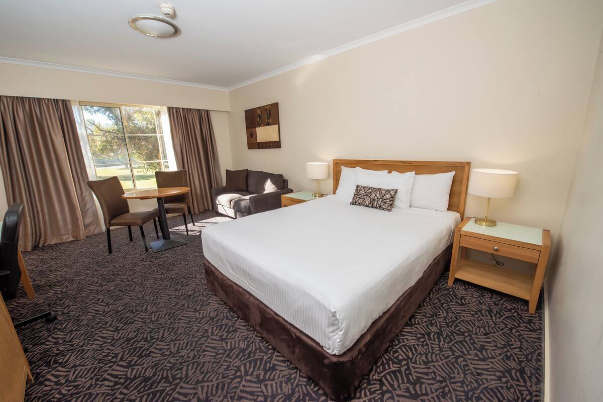 A hotel room with a large bed, a desk, a chair, and a window with curtains.