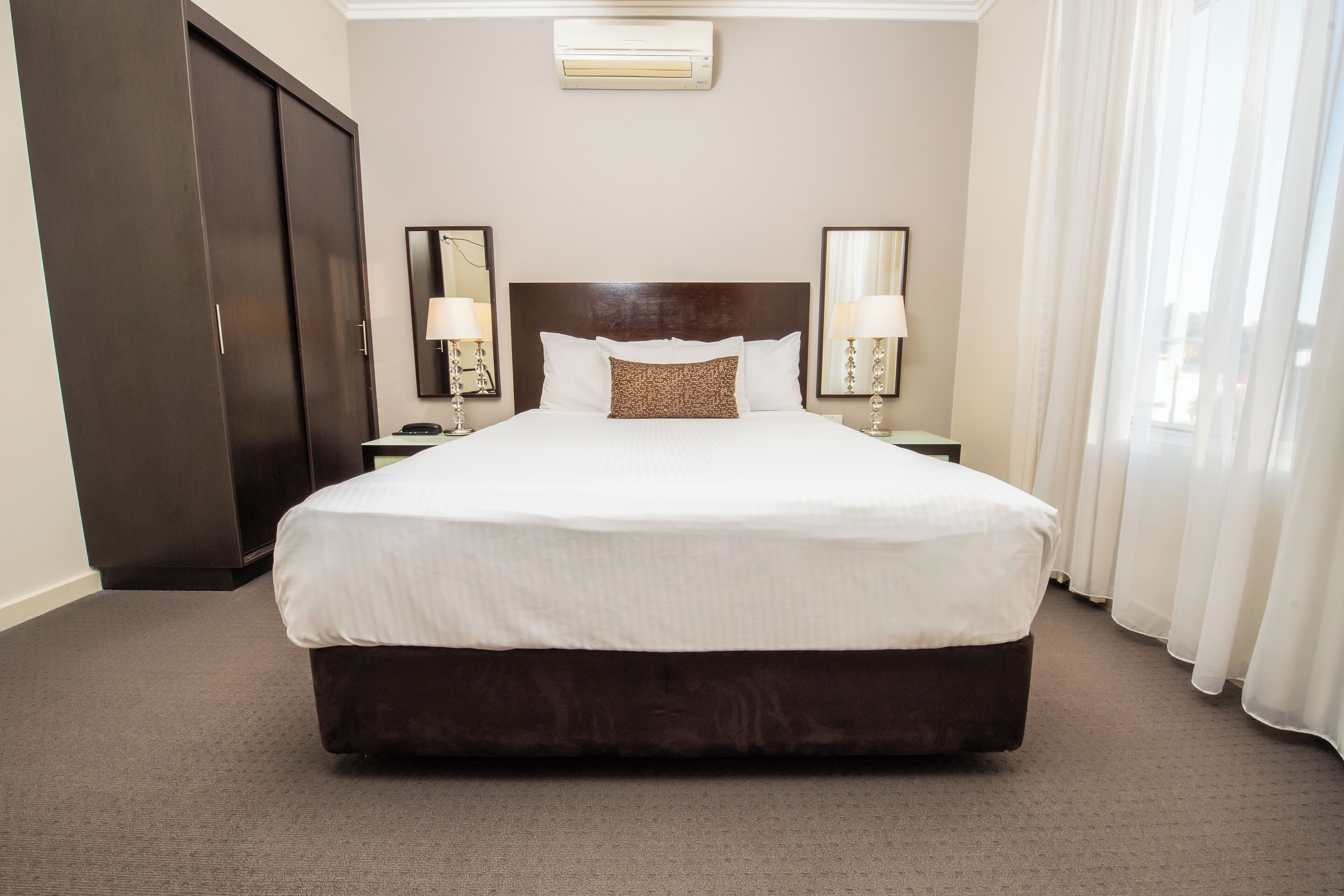A hotel room with a large bed, two bedside tables with lamps, a wardrobe, and a window with curtains.