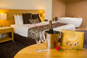 Habitación de hotel con cama, mesita de noche con lámpara, una botella de champán en cubos, dos copas y una caja de bombones Lindor.
