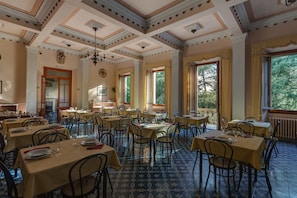 A dining area with multiple tables and chairs, large windows, and a decorative ceiling. - Giotto Park Hotel (Vaglia)