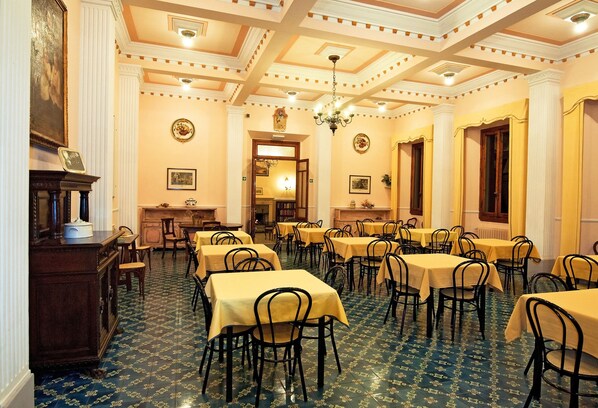 Comedor con mesas dispuestas para comensales, una araña y un suelo con diseño.