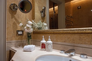A bathroom with a sink, two bottles of hand wash, a towel, a mirror, and a vase with flowers. - Palazzo Excelsior - The Leading Hotels of the World (Palermo)