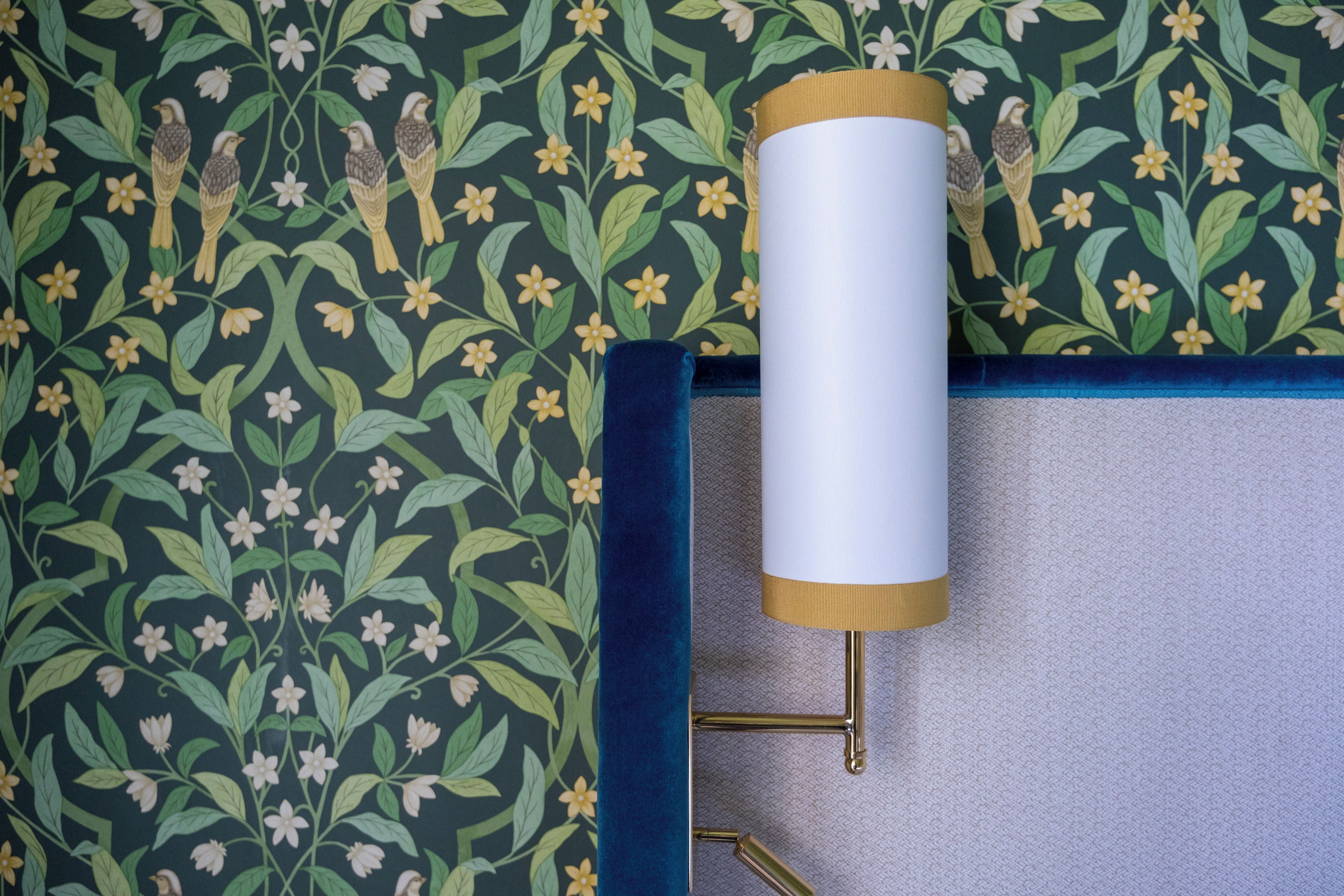 Eine Wand mit einem floralen Muster und einer Lampe mit goldfarbenem Fuß.