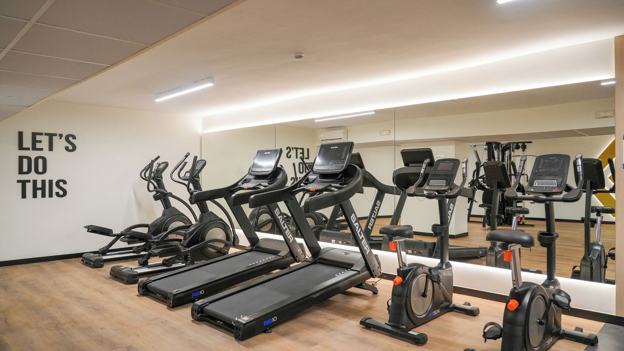 Une salle de sport équipée de nombreux appareils de cardio, d’un mur d’encouragement et d’un grand miroir.