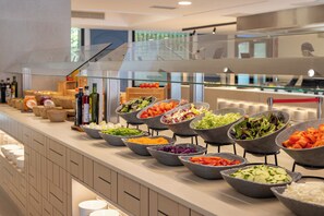 Un bufé con diversas opciones de comida, una baranda de vidrio y vistas al área de la cocina.