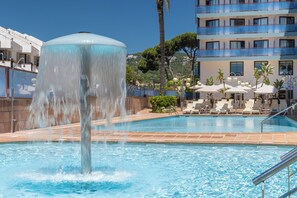 Une piscine avec une fontaine, des chaises longues et un bâtiment doté de balcons en arrière-plan.