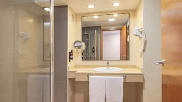 A bathroom with a glass shower enclosure, a sink with a mirror above it, and a towel rack with two towels.