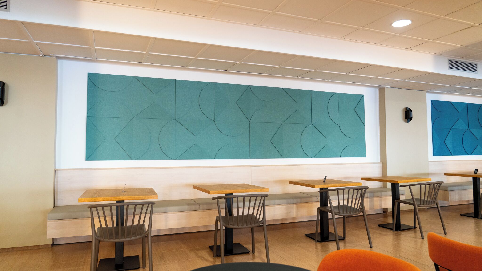 A modern interior with a seating area featuring tables and chairs, a large geometric wall design, and a ceiling with recessed lighting.