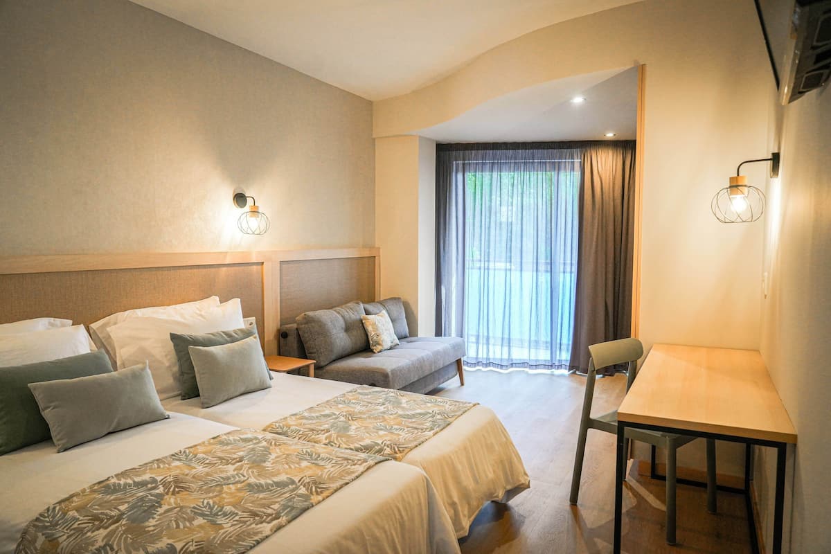 A hotel room with two beds, a sofa, a table, and a chair.