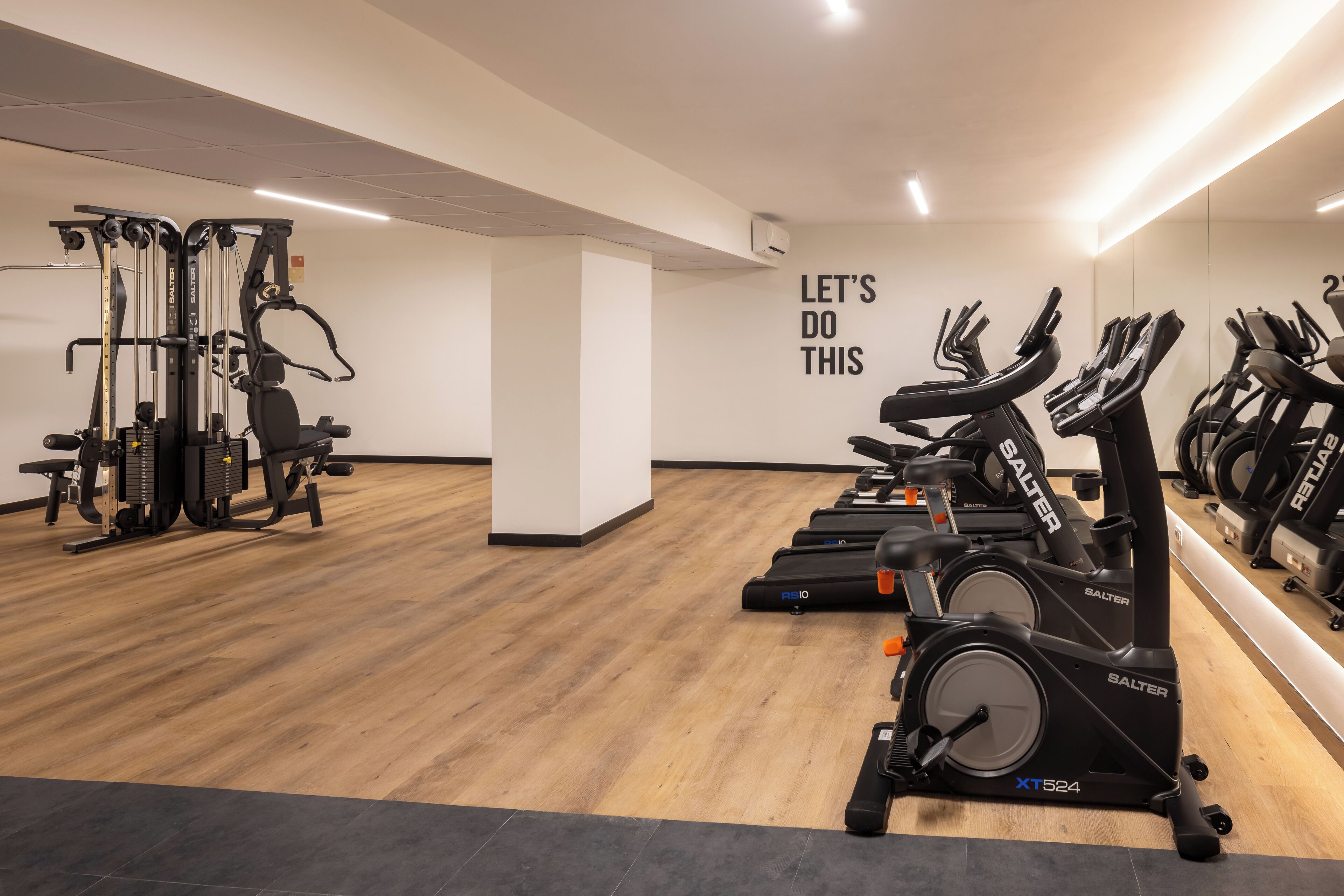 A gym with exercise machines, a motivational wall, and a wooden floor.