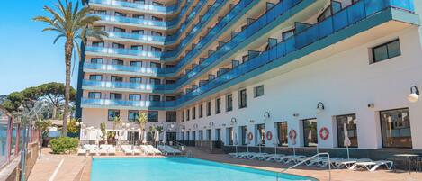Um hotel com piscina, várias varandas e espreguiçadeiras.