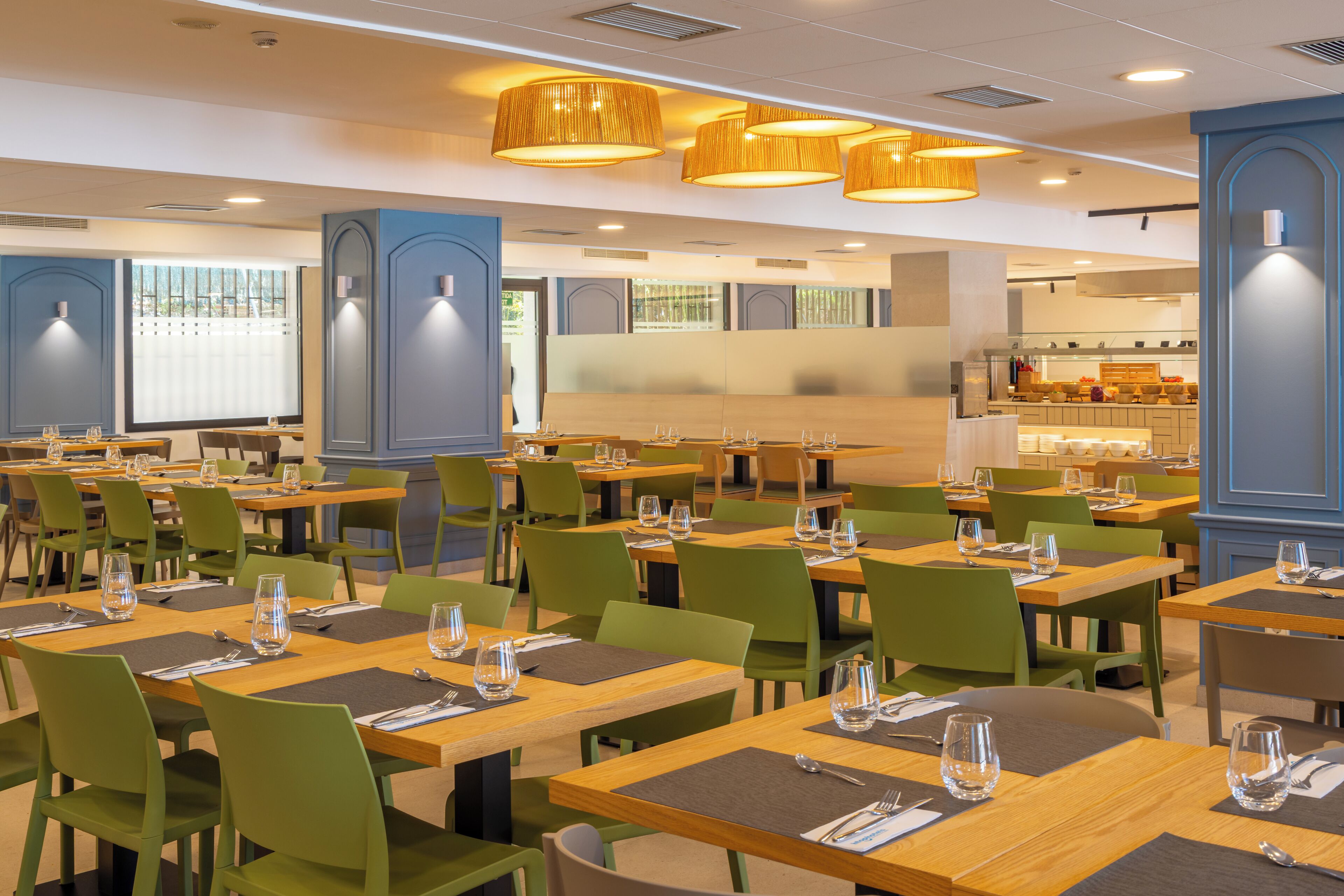 A restaurant with multiple tables and chairs, a kitchen area, and large windows.