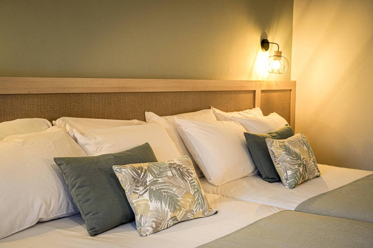 A hotel room with a large bed, multiple pillows, and a wall-mounted light fixture.