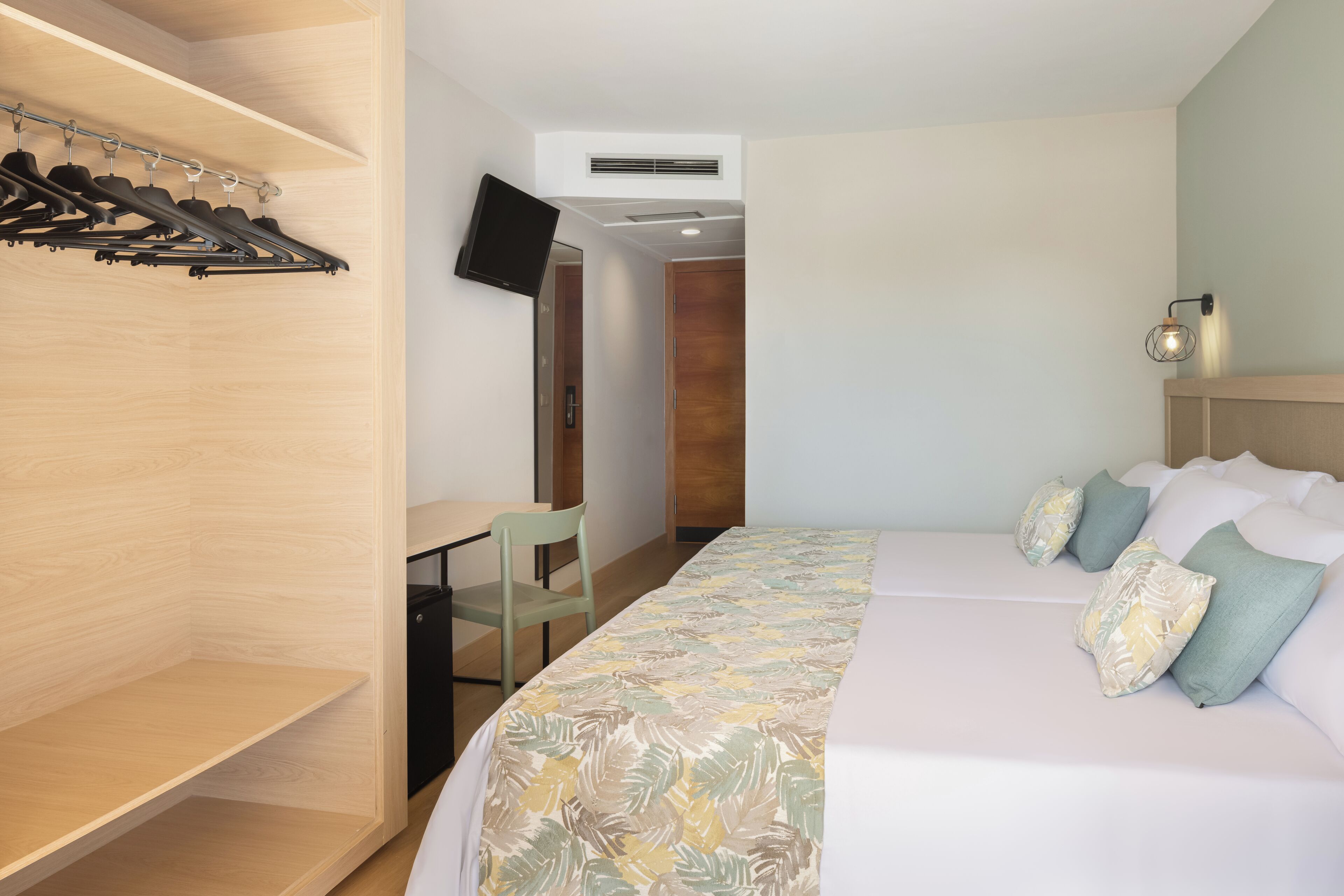 Una habitación de hotel con cama, escritorio, televisor y armario.
