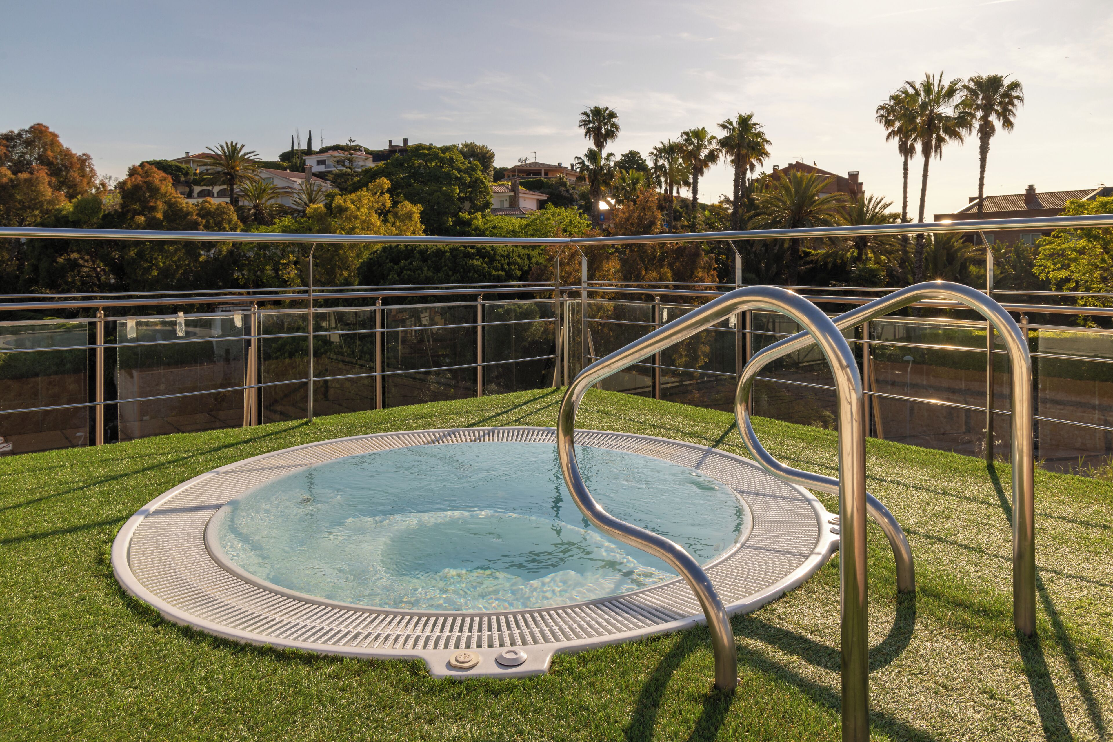 Una piscina con una escalera de metal, rodeada por una cerca de metal y un área con césped.