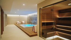 Un área de spa moderna con piscina climatizada, suelo de madera y sauna con paredes de vidrio.