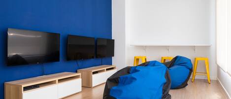 A modern living room with a blue accent wall, two flat-screen TVs, a wooden entertainment unit, and two bean bags.