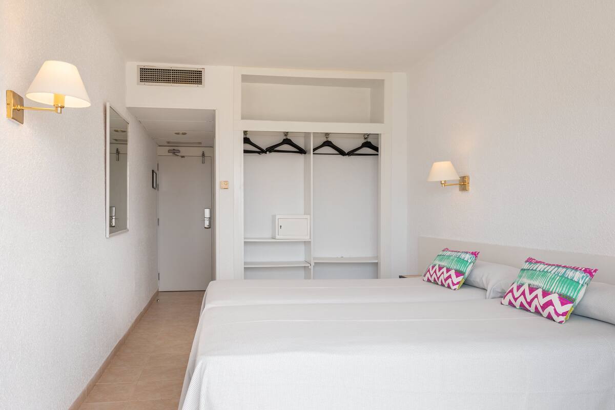 Un dormitorio con una cama, dos almohadas, un armario y dos lámparas de pared.