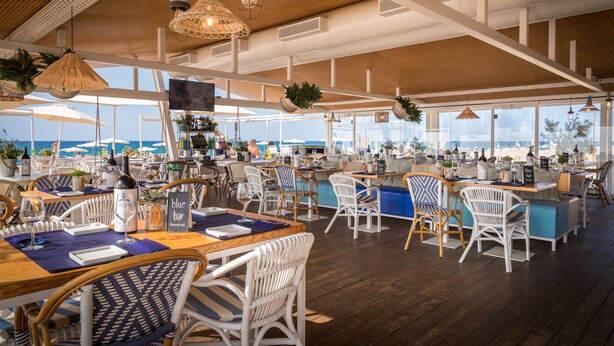 Un restaurant amb sostres alts, mobles de vimetla i vista a la platja.
