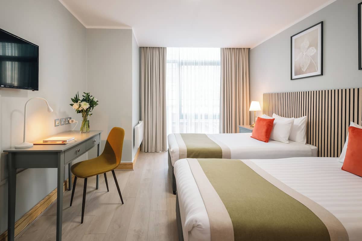 Habitación de hotel con escritorio, silla, dos camas, televisor y ventana con cortinas.