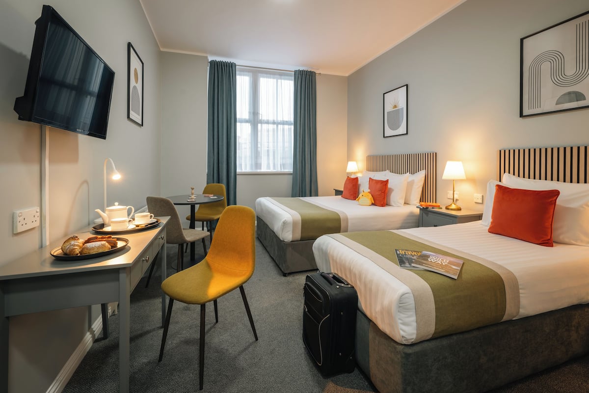 Habitación de hotel con dos camas, un escritorio con silla, una mesa con lámpara y una televisión.