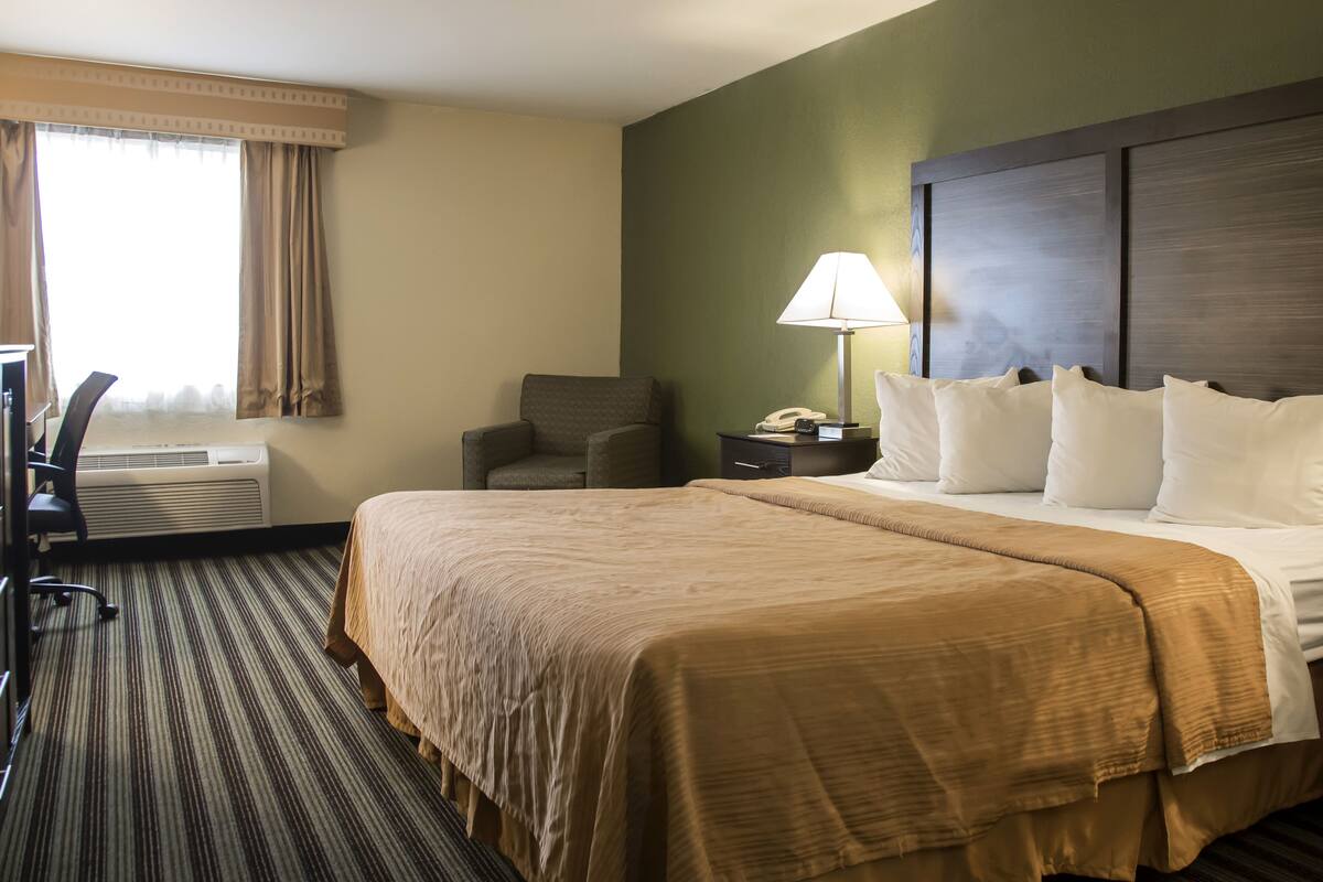 A hotel room with a large bed, a desk with a chair, a lamp, and a telephone.