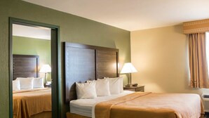 A hotel room with a large bed, a bedside table with a lamp, a mirror, and a window with curtains. - Quality Inn & Suites Loves Park near Rockford (Loves Park)