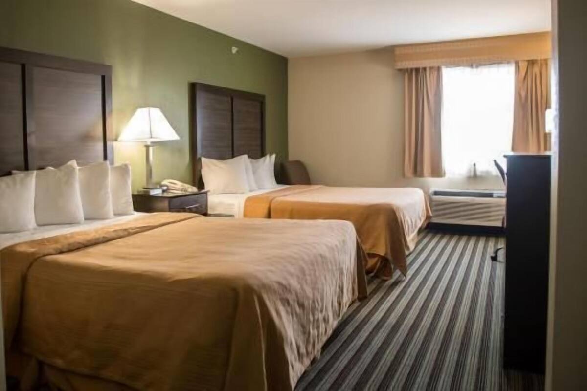 A hotel room with two beds, a desk, a lamp, and a window with curtains.